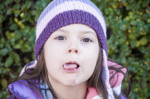 Sweet little girl in purple jacket and woolen purple hat having fun in the playground