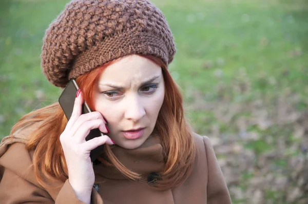 Seductive young redhead talking over the mobile phone in the public park