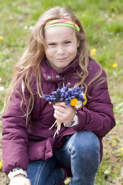 Little girl in purple jacket holding a flowers in the park
