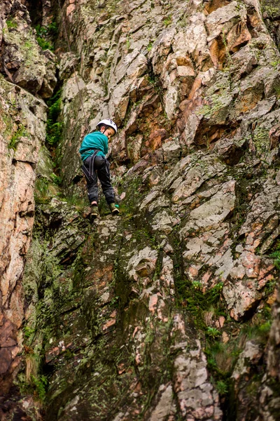 Der kleine Junge mit dem Helm erklimmt den Felsen, der kleine Bergsteiger treibt Sport im Freien. — Stockfoto