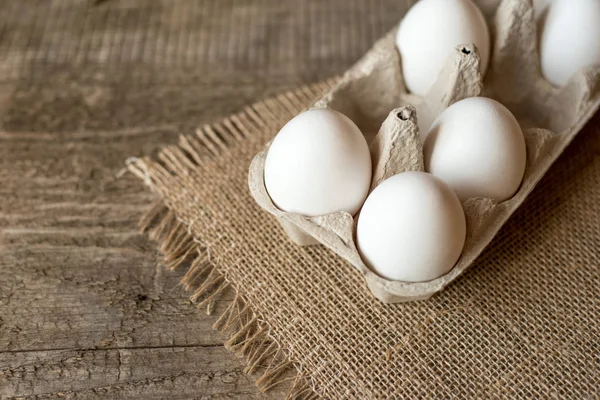 Raw eggs in egg box on wooden background.
