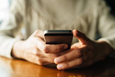 Kafedeki ahşap masada akıllı telefon kullanan bir kadın.