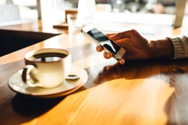 Kafedeki ahşap masada akıllı telefon kullanan bir kadın.