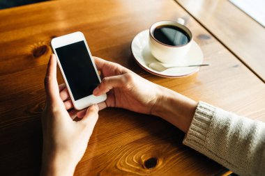 Kafedeki ahşap masada akıllı telefon kullanan bir kadın.