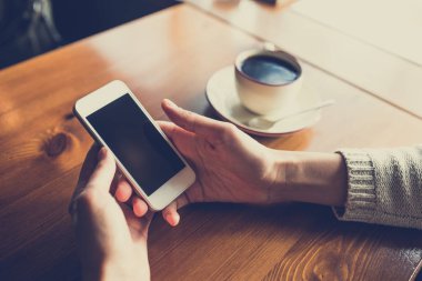 Kafedeki ahşap masada akıllı telefon kullanan bir kadın.