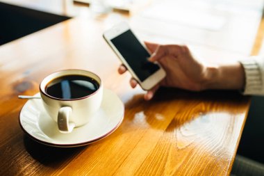Kafedeki ahşap masada akıllı telefon kullanan bir kadın.