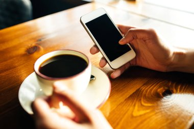 Kafedeki ahşap masada akıllı telefon kullanan bir kadın.