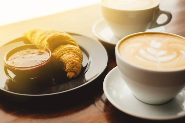 Two cups of cappuccino and croissant with jam