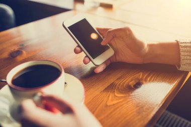 Kafedeki ahşap masada akıllı telefon kullanan bir kadın.