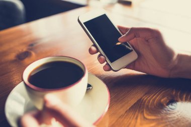 Kafedeki ahşap masada akıllı telefon kullanan bir kadın.