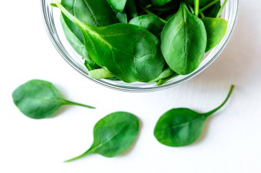 Beyaz masada cam kase taze yeşil ıspanak yaprakları.