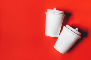 Kırmızı arka plan üzerinde iki beyaz kağıt bardak.