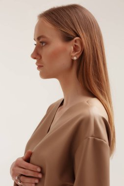 Temiz ciltli güzel bir genç kadın. Mükemmel makyaj. Güzellik modası. Kozmetik göz farı. Küpeli ve çantalı pürüzsüz saç, sade arka planda doğal aksesuarlar.