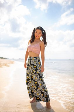 Muhteşem, mega mutlu Asyalı kız. Arka planda deniz dalgaları ve ufuk ile duygusal poz veriyor. Güneş gözlüklü güzel siyah saçlı kız mutluluğunu ifade ediyor..