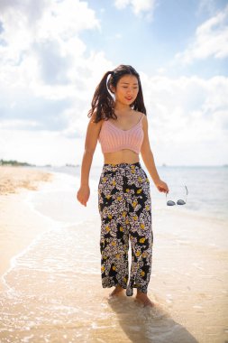 Muhteşem, mega mutlu Asyalı kız. Arka planda deniz dalgaları ve ufuk ile duygusal poz veriyor. Güneş gözlüklü güzel siyah saçlı kız mutluluğunu ifade ediyor..