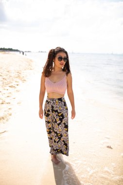 Muhteşem, mega mutlu Asyalı kız. Arka planda deniz dalgaları ve ufuk ile duygusal poz veriyor. Güneş gözlüklü güzel siyah saçlı kız mutluluğunu ifade ediyor..