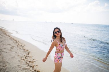 Muhteşem, mega mutlu Asyalı kız. Arka planda deniz dalgaları ve ufuk ile duygusal poz veriyor. Güneş gözlüklü güzel siyah saçlı kız mutluluğunu ifade ediyor..