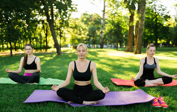  Happy woman doing yoga exercises, meditate in the park. Yoga meditation in nature. Concept of healthy lifestyle and relaxation. Pretty woman practicing yoga on the grass