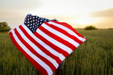 Pembe bluzlu, beyaz, genç, güzel, güzel bir kız. Üzerinde Amerikan bayrağı olan kot pantolonlar. Gün batımı manzaralı yeşil buğday tarlasında. Bağımsızlık Günü