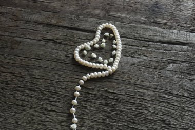 Ahşap arka plan üzerinde küçük beyaz çiçek ve bir kalp şeklinde inci boncuk Üstten Görünüm