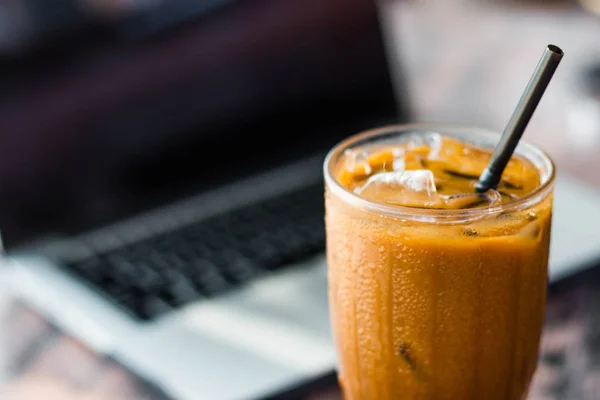 Eiskaffee in einer Tasse mit einem Laptop im Hintergrund. Freiberufler Konzept und Arbeit an Urlaubsidee. — Stockfoto