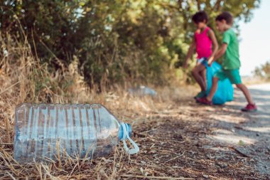 Çocuklar ormanda plastik torbayla çöp topluyorlar. Gönüllülük, yardım laşma ve ekoloji kavramı.