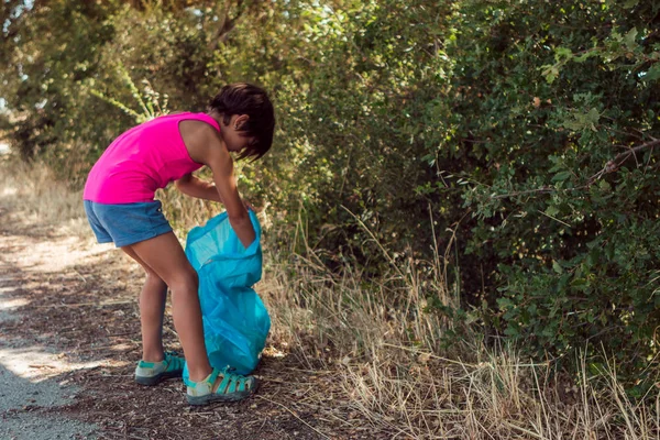 Niña haciendo tareas escolares y recogiendo basura en una zona rural — Foto de Stock