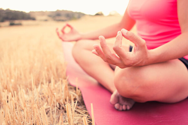Close up hands of a young woman wearing sport clothes meditating and doing yoga peacefully in a open field
