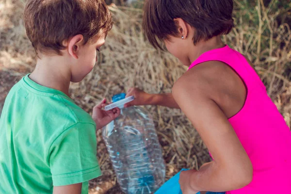 Dos niños recogiendo basura en el bosque. Voluntariado, caridad, tareas escolares y concepto de ecología . — Foto de Stock