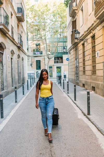 Jonge mooie Latijnse vrouw toerist met een reiskoffer arriveert in een nieuwe stad op vakantie — Stockfoto