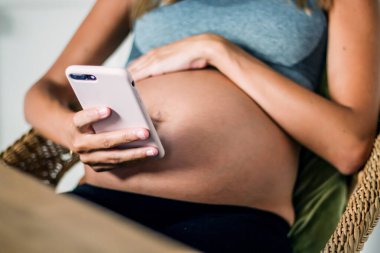 Güzel hamile bir kadının evde dinlenirken cep telefonunu kullanması.