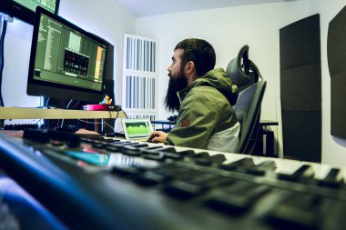 Uzun sakallı genç DJ stüdyosunda elektronik müzik yapıyor..