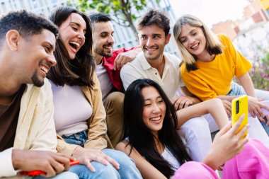 Bir grup çok ırklı insan cep telefonu uygulamasından komik içerikler izliyor. Gençlik, sosyal medya ve teknoloji kavramı