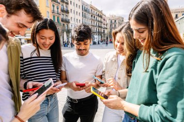 Mutlu öğrenciler dışarıda cep telefonları kullanarak, içeriği paylaşarak ve gülümseyerek eğleniyorlar. Gençlik ve teknoloji yaşam tarzı konsepti