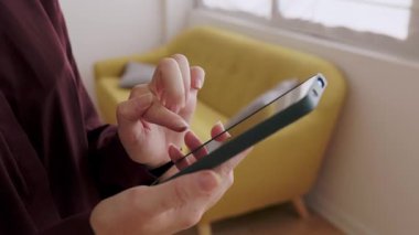 Evde arka planda kanepesi olan cep telefonu dokunmatik ekranı kullanan tanınmayan bir kadını kapat.