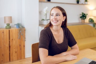 Genç, güzel, kızıl saçlı bir kadın uzak çalışma günlerinde dizüstü bilgisayarı ile masada oturuyor.