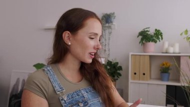 Masada oturmuş video görüşmesi için laptop kullanan sıradan bir yetişkin kadın. İnternette çalışıyor ya da evde rahat bir ofis ortamında çalışıyor olabilir. Uzak çalışma ve eğitim yaşam tarzı kavramı.