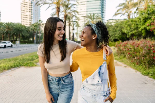 Şehir caddesinde yürürken dışarıda birlikte gülen iki çok ırklı kadın arkadaş.