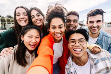 Bir grup genç öğrenci dışarıda telefonla selfie çektiriyorlar. Gençlik toplumu ve uluslararası arkadaşlık kavramı