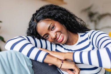 Evdeki rahat kanepesinde dinlenen gülümseyen genç bir zenci kadının portresi.