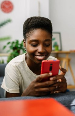 Kanepede uzanmış, cep telefonu kullanan, evde boş vakitlerin tadını çıkaran, sosyal medyada gezinen ya da arkadaşlarıyla sohbet eden genç bir kadının dikey görüntüsü. Teknoloji ve gençlik kavramı