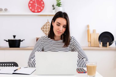 Young woman using laptop while sitting at home kitchen. Female student attending training course class, listening teacher through web conference call. Education or business concept