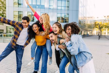Group of cheerful multiracial friends posing outdoors, stacked on each other back and smiling. Friendship, youth, and joyful lifestyle concept.