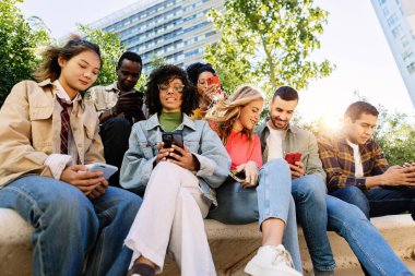 Multiracial youth using smart phone while hanging out in urban street, enjoying connection, friendship and modern student lifestyle.