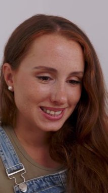 Vertical HD video of happy spanish redhead woman using smartphone, browsing internet, checking social media, ordering online, shopping, playing mobile games or texting while relaxing on couch