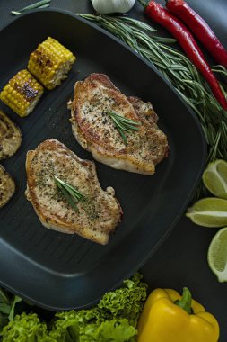 Rosemary ile dekore edilmiş bir tavada sebzeli ızgara biftek. Taze yeşillik. Marul, tatlı biber, roka ve biberiye dalları. Koyu arka plan. Yukarıdan görüntülemek.