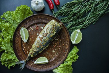 Bir teralka üzerinde kızarmış uskumru baharat için balık ve yeşillik ile dekore edilmiştir. Doğru beslenme. Koyu arka plan. Yukarıdan görüntülemek.