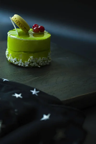 Un pequeño pastel de pistacho con una capa verde y decorado con viburnum, aderezo de confitería sobre un fondo negro. Vista lateral . — Foto de Stock