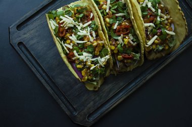 Fotoğraf bir ahşap tahta üzerinde et, peynir, Mısır, soğan ve domuz eti otlar ile Meksika Taco. Ketçap sosu ve acı biber. Siyah arka plan. Yukarıdan görüntülemek