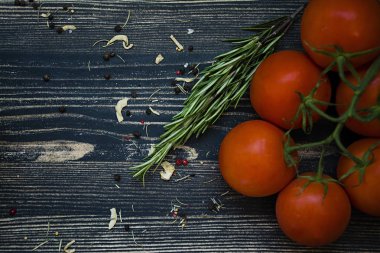 Fresh tomatoes with a branch of rosemary. Dark wooden background. View from above.